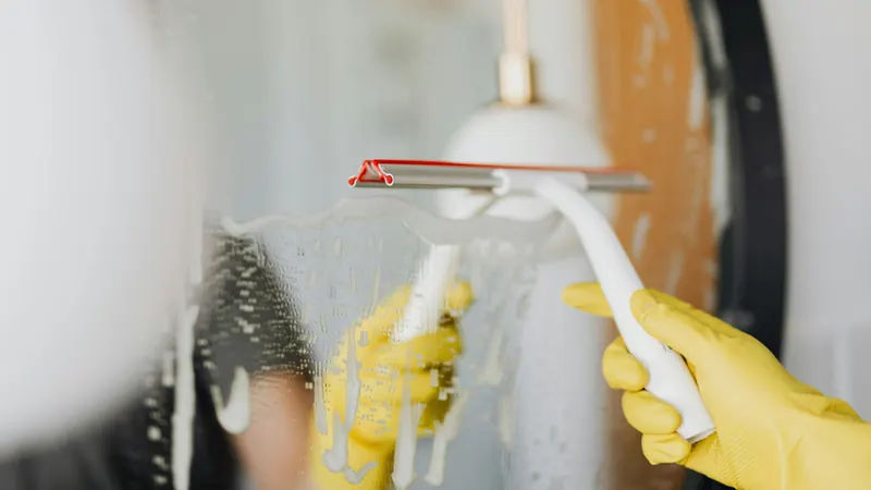 Gloved cleaner using a squeegee on a soapy glass surface