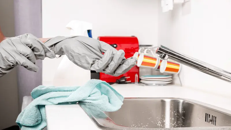 Gloved cleaner spraying a kitchen sink
