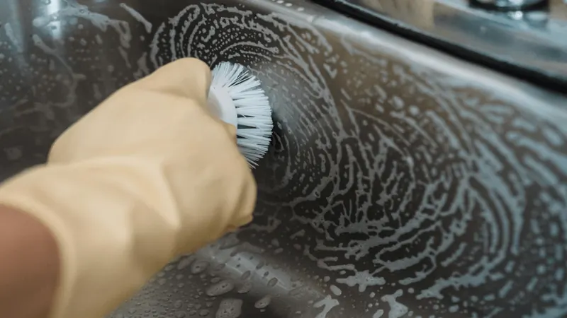 Gloved cleaner scrubbing a soapy sink