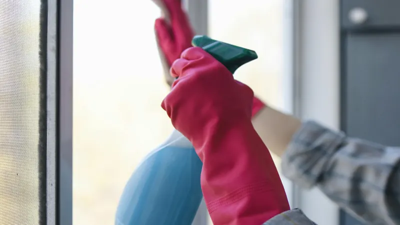 Gloved cleaner spraying an interior window